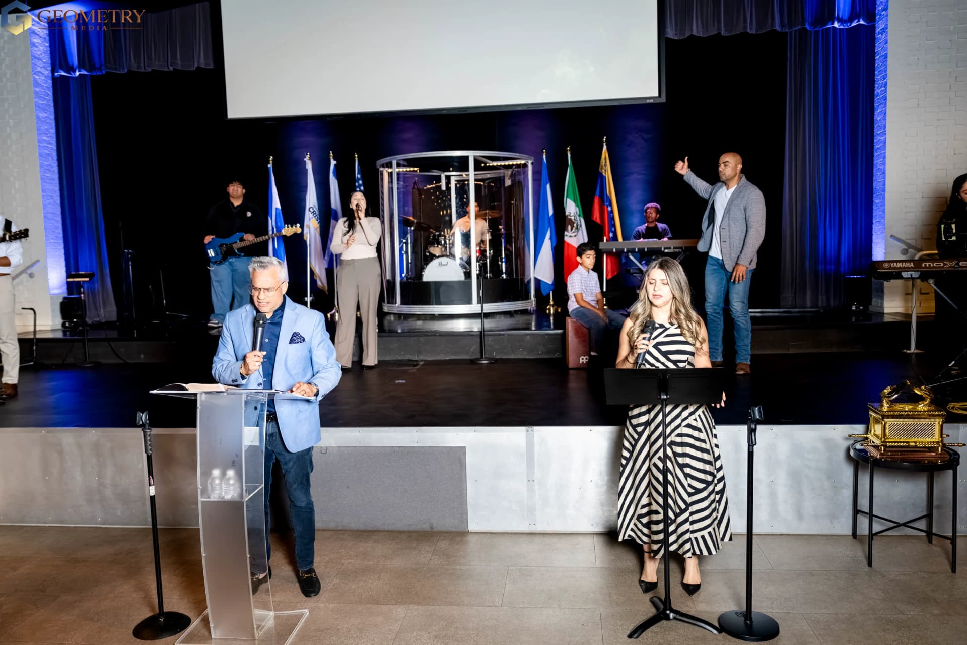 International church speakers on a stage framed by flags in Dallas-Fort Worth